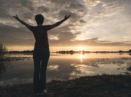 young slim woman meditating on the banks of the lake at sunset