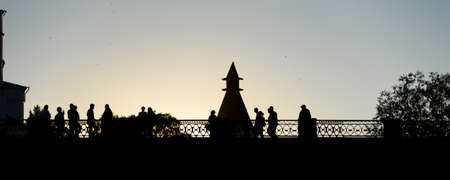 Silhouettes of people walking across the bridge against the sky