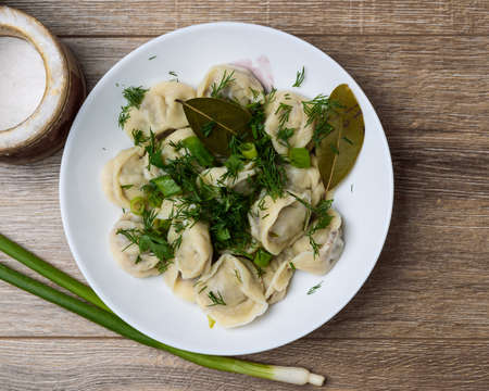 plate of traditional Russian dumplings sprinkled with herbs on a wooden tableの写真素材