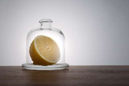 half of lemon in glass bell jar on wooden table on light backgroundの写真素材