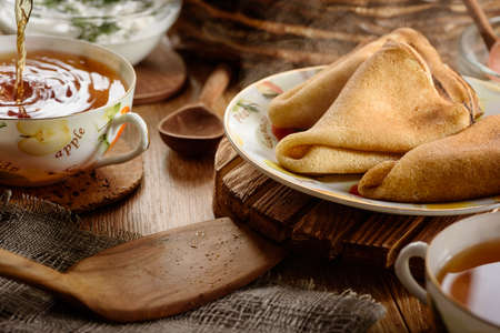Breakfast tea being poured into a Cup and hot ruddy delicious pancakes on wooden tableの写真素材