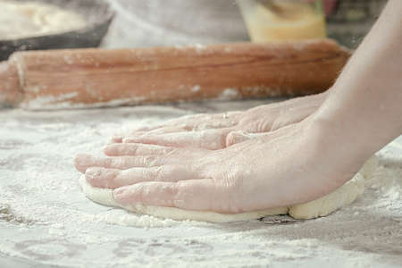 female hands in flour kneading dough on table