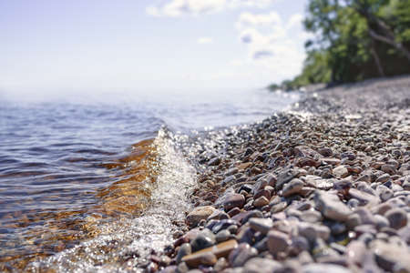 Sea wave is lapping on pebble beach against sea and blue sky in the blurの写真素材