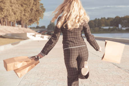 back view of a woman jumping with shopping bags. Girl in a the pantsuit runs away with paper bags in their hands.の写真素材