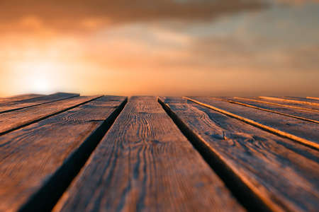 Horizontal shot. Close up top wooden table and blur sunset background. Tonted orange.の写真素材