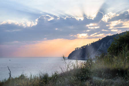 Quiet evening at sea. The suns rays illuminate the sea and the mountains covered with forest.の写真素材