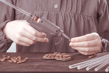 Hobby concept baby hands close up with glue gun. Photo toned red.