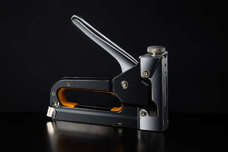 Horizontal shot of construction stapler on black background with reflection.