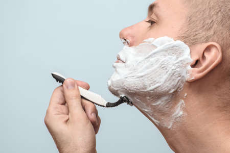 Crop shot of a man shaving with a razor on a grey background. Side view. Photo with copy space.の写真素材