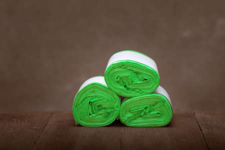 Three roll green eco garbage bag end view isolated on brown wooden background.
