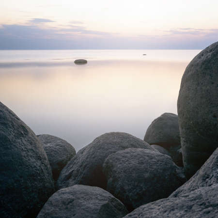 Square shot of stones on the background of the sea at sunset tonted with orange. The picture was taken at a long exposure.の写真素材