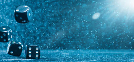 Horizontal shot of several black cubes falling on a blue background illuminated by bright light. . The concept of gambling. Photo with copy space.の写真素材