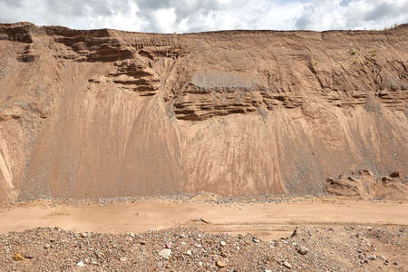 The road at a sand quarry on the background of sandy mounds and sky.