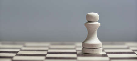 One white pawn close-up on a chessboard on a gray background. Background in blur.
