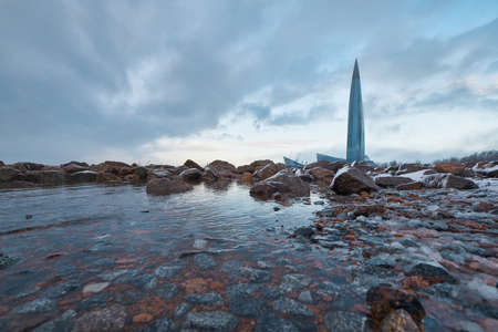 Lakhta center on a background of cloudy sky and large stones covered with frost and ice.の写真素材