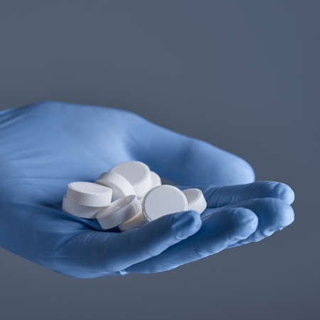 Hand in blue medical glove hold white pills on a gray background.の写真素材