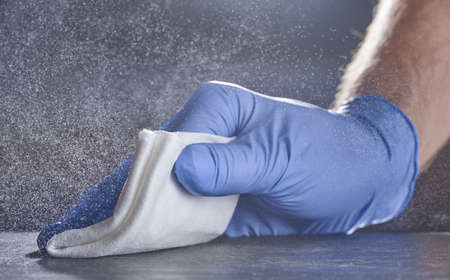 A hand in a medical glove wipes the table. Grey background with splashes of disinfectant.の写真素材