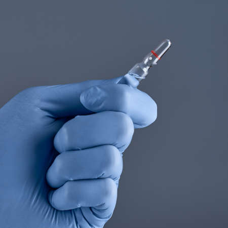 Hand in medical blue glove holding ampoule. Concept of medical help.の写真素材