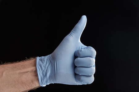 Horizontal shot of hand in a medical glove with thumb up isolated on black background. Ok sign by medical worker.の写真素材