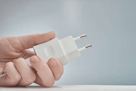 Horizontal shot of white electric adapter in a hand, isolated on the gray.
