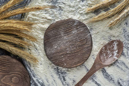 Horizontal shot of wheat flour, wheat ear, cutting board and wooden spoon on wooden background, top view. Photo with copy space.の写真素材