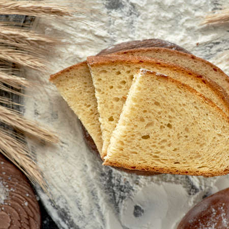 Square shot of slices of bread on a wooden table sprinkled with flour. Wheat ears on the sides.