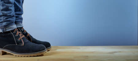 Horizontal shot of female legs in demi-season boots and blue jeans on wooden floor on a blue background. Fashion background.の写真素材