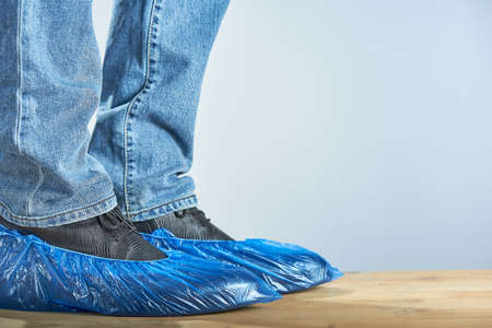 Horizontal shot of men's legs in blue shoe covers worn over classic shoes on gray background, closeup. Photo with copy space.の写真素材