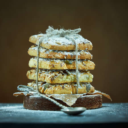 Square shot of cookies with nuts and seeds are sprinkled with powdered sugar on a brown background.の写真素材