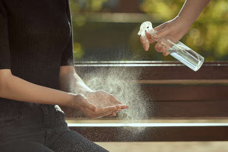 Horizontal shot of female hands are treated with a sanitizer girl's hands against the background of bench. A mother treats her daughter's hands with sanitizer.の写真素材