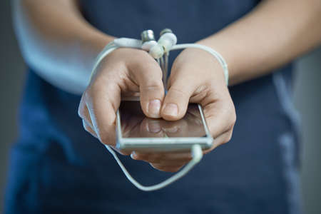 Horizontal shot of hands tied with earphone wire. In the hands of the phone. The concept of dependence on gadgets.の写真素材