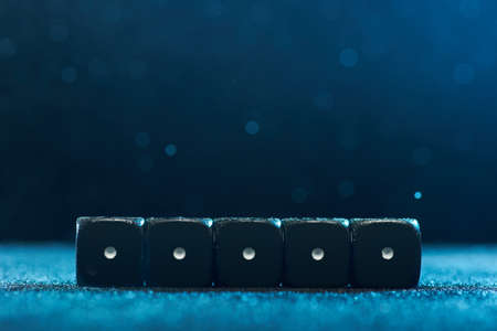 Horizontal shot of five identical black dice on a blue background. The concept of gambling. Photo with bokeh.の写真素材