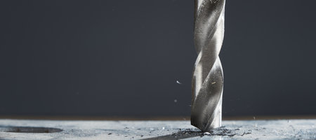 Metal drill bit make holes in metal billet on industrial drilling machine with shavings.