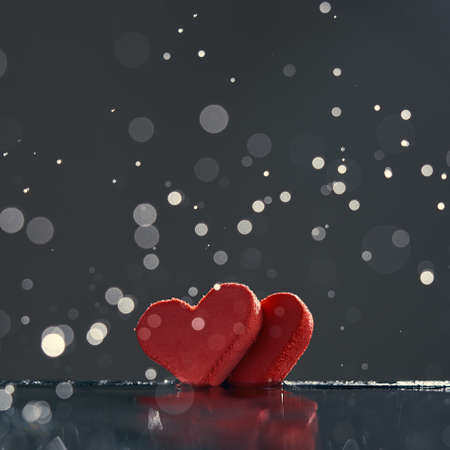 Two red hearts with rain drops reflected in the water on a dark background with a bokeh. Photo with...
