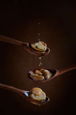 White pickled mushrooms on wooden spoons on dark background. Pickled mushrooms are watered with olive oil. Drops of oil flow down.の写真素材