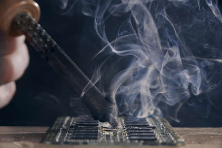 Backdrop of smoking soldering iron on dark background. The concept of an unsuccessful computer repair.の写真素材