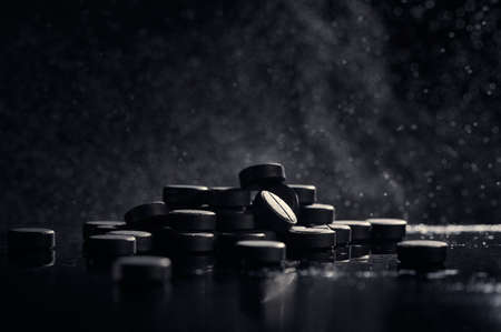 Activated carbon tablets on a black background with a side. The concept of cleansing the body. Pharmaceutical background.の写真素材