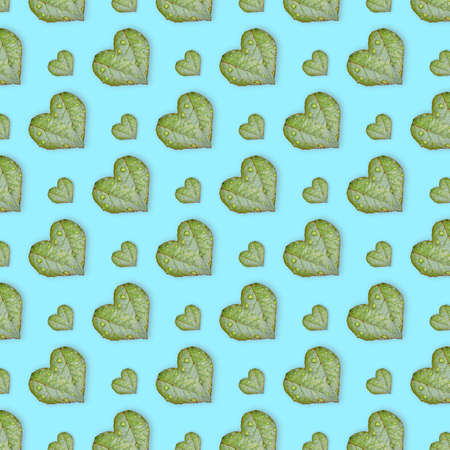 Green leaves in the shape of heart seamless pattern on blue background. The concept of love.