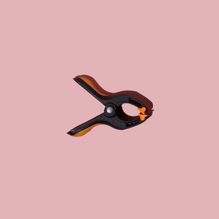Plastic spring clamp isolated on pink background. Working hand tool. Black and orange spring clamp. Closeup.の写真素材