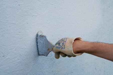Horizontal shot of hand in a work glove paints the wall of the house with blue paint.の写真素材