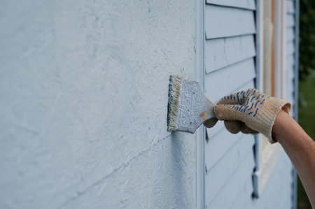 Horizontal shot of hand in a work glove paints the wall of the house with blue paint.の写真素材
