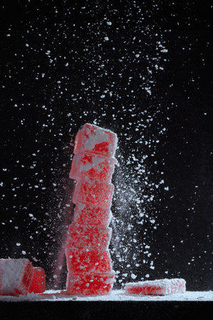 Vertical shot of strawberry red marmalade jelly candy's covered with powder sugar on black background. Powdered sugar is sprinkled on berry marmalade on a black background.の写真素材