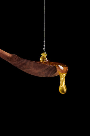 Vertical shot of honey pouring on wooden spoon and dripping from spoon. dark background.の写真素材