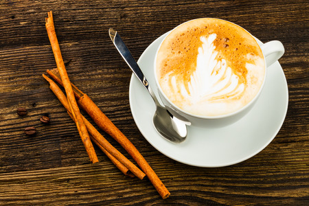 cup of cappucino, cinnamon stick and coffee bean isolatad on wooden backgroundの写真素材