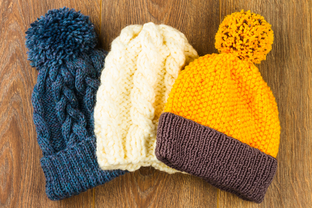 yellow, white and gray knitting caps on wooden background