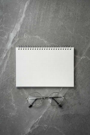 open notebook with glasses on grey marble table top view, spiral notepad on gray office desktop. clear to do list, flat lay.の写真素材