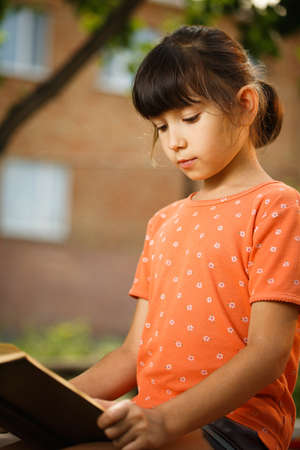 Cute girl in T-shirt is reading outdoors on an sunny day. Preparation for school and international...