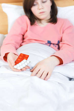 little girl is sick and lies in bed, next to them are tablets with a gradus. The child has a fever, cold and flu. treated at homeの写真素材