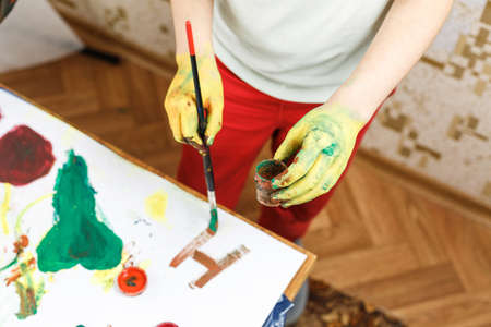 little girl paint with hands on the table, drawing lesson at school. schoolchildrens hands are painted with paintの写真素材