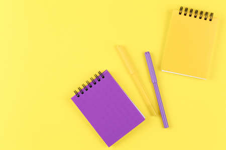 closed notebooks with markers on isolated yellow background flat lay. top view. school concept, a notebook with a spiral lies on a bright orange tableの写真素材